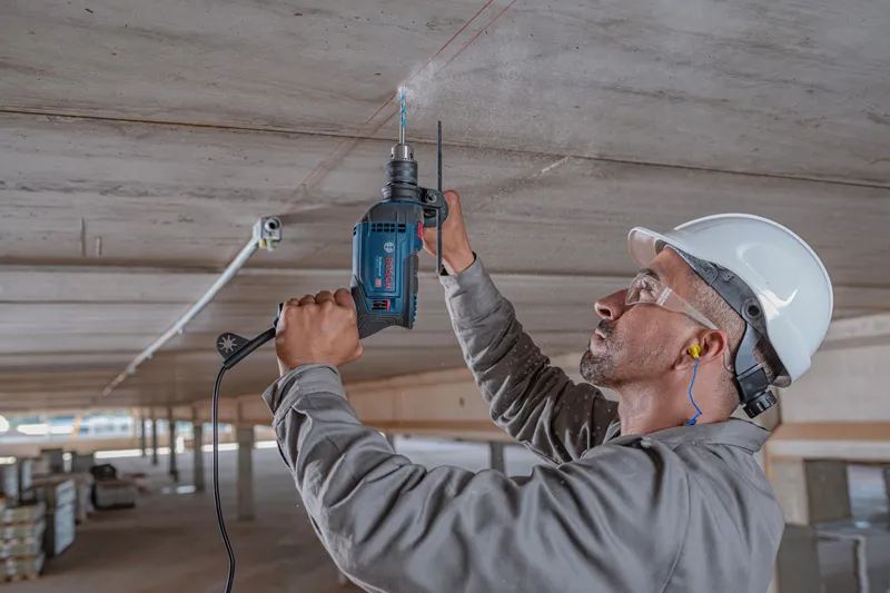Una persona que usa equipo de seguridad perfora un techo de concreto usando un taladro de impacto.