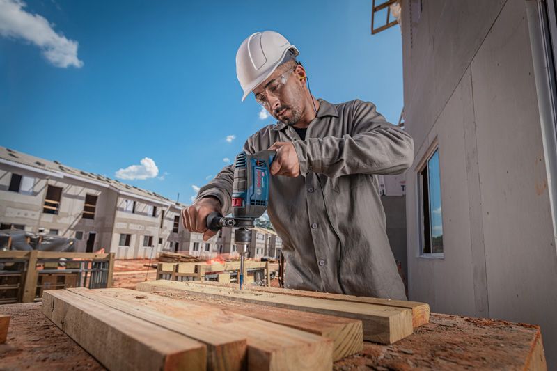 Una persona que usa equipo de seguridad perfora vigas de madera en un sitio de construcción.