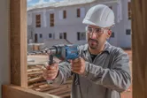 Una persona que usa equipo de seguridad perfora madera en un sitio de construcción.