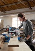 Una persona que usa equipo de seguridad corta madera con una sierra ingletadora en un taller.