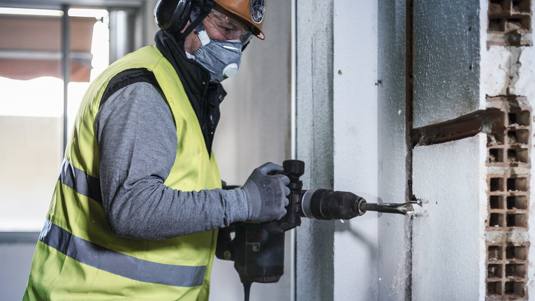 Una persona que lleva equipo de seguridad perfora una pared de hormigón.