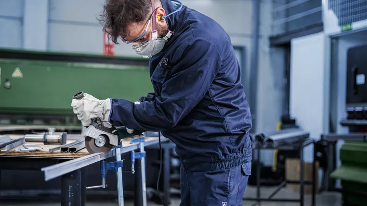 Una persona que usa equipo de seguridad utiliza una amoladora angular para cortar una barra de metal.