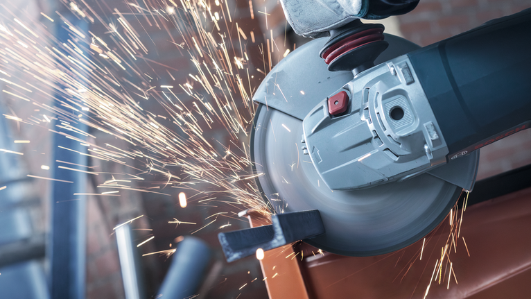 Una persona que usa equipo de seguridad muele metal, creando chispas brillantes.