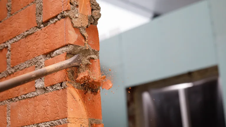 Herramienta de cincel que rompe una pared de ladrillos rojos durante la demolición.