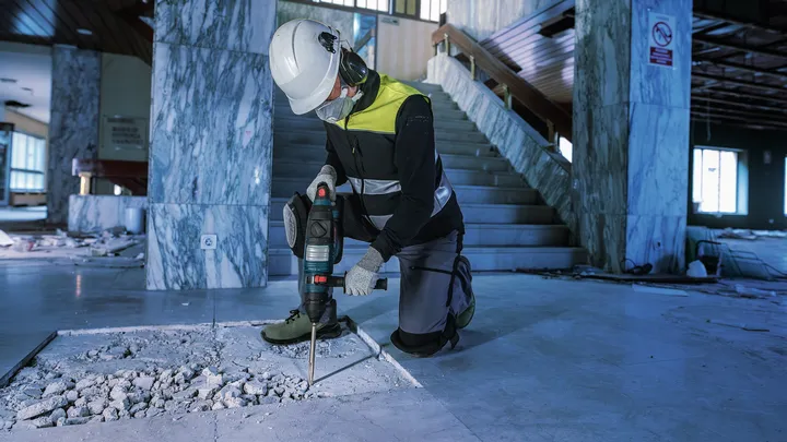 Una persona que usa equipo de seguridad utiliza un martillo demoledor para romper el hormigón en un interior.