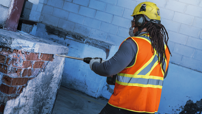 Una persona que usa equipo de seguridad utiliza una herramienta de demolición para romper hormigón y ladrillos.