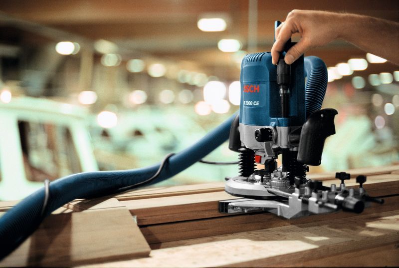 Persona que opera una fresadora con una manguera de extracción de polvo sobre tablones de madera.