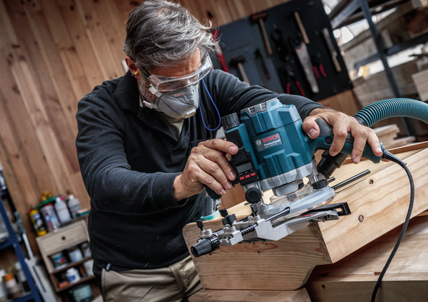 Una persona que usa equipo de seguridad utiliza una fresadora para dar forma al borde de una tabla de madera.