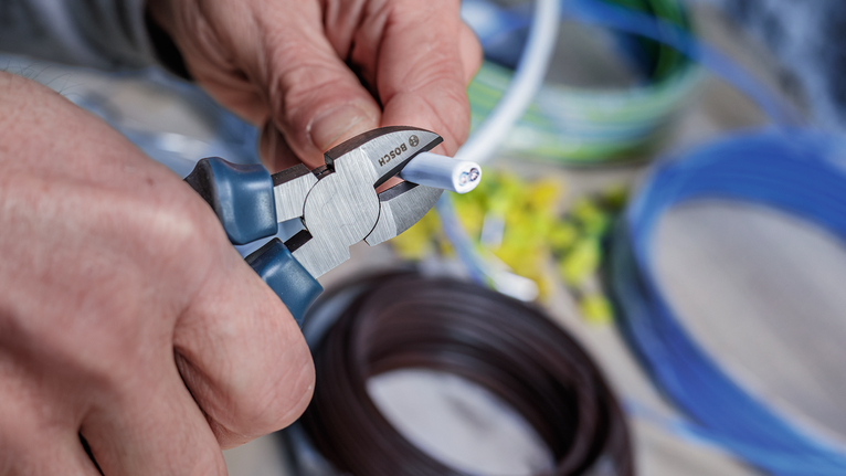 Una persona corta un cable eléctrico con unos alicates.