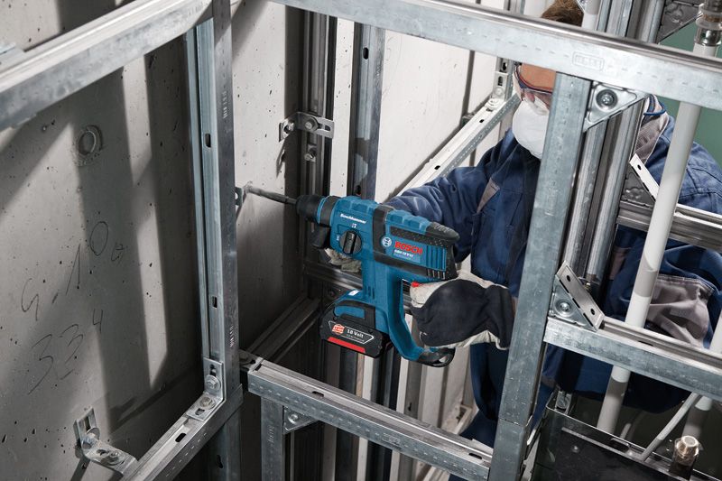 Una persona que usa equipo de seguridad perfora una pared de hormigón utilizando un martillo perforador inalámbrico.