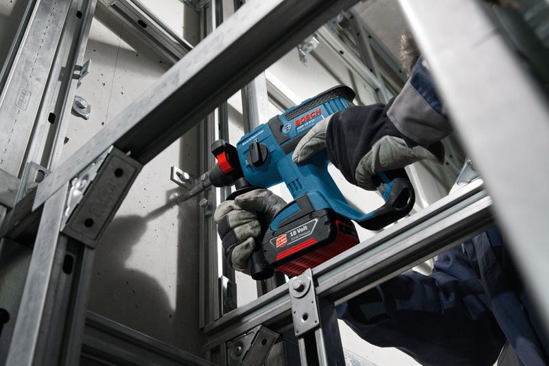 Una persona que usa equipo de seguridad perfora una pared de hormigón utilizando un martillo perforador inalámbrico.