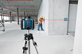 Un trabajador, equipado con material de seguridad, alinea una pared utilizando un nivel láser montado sobre un trípode.