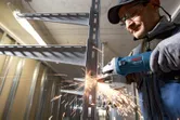 Una persona que usa equipo de seguridad corta estanterías de metal con una amoladora angular, saltando chispas.