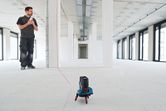 Persona utilizando un nivel láser para proyectar líneas rectas en una habitación sin terminar.