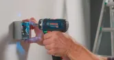 Una persona utiliza un taladro inalámbrico para fijar tornillos en una caja eléctrica en la pared.