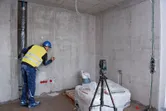 Una persona que usa equipo de seguridad marca una pared utilizando una herramienta niveladora láser en un trípode.