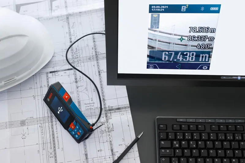 Medidor láser conectado a un ordenador situado encima de planos técnicos.