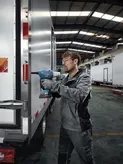 Un trabajador que usa equipo de seguridad usa un taladro inalámbrico para fijar metal a un remolque.