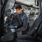 Una persona que usa equipo de seguridad utiliza una herramienta eléctrica para ensamblar la puerta de un automóvil en una fábrica.