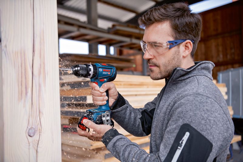 Una persona que usa equipo de seguridad perfora una viga de madera en un taller.