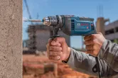 Una persona que usa equipo de seguridad perfora hormigón con un taladro de impacto.