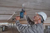 Una persona que usa equipo de seguridad perfora un techo de concreto usando un taladro de impacto.