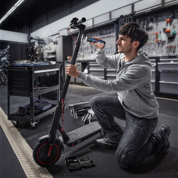 Una persona se arrodilla y usa un destornillador inalámbrico para reparar un scooter eléctrico.