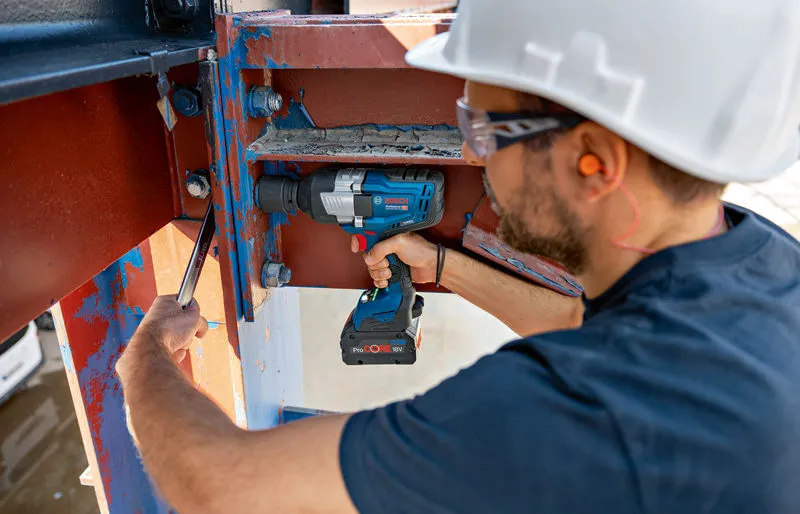 Una persona que usa equipo de seguridad utiliza una llave de impacto inalámbrica sobre una viga de acero.