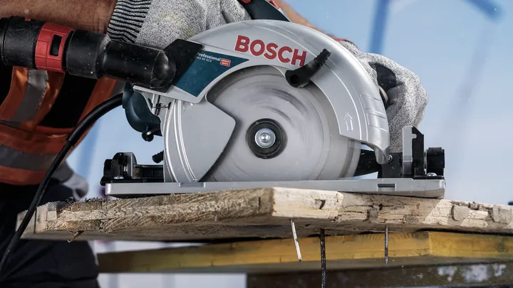 Una persona que usa equipo de seguridad utiliza una sierra circular para cortar una tabla de madera.