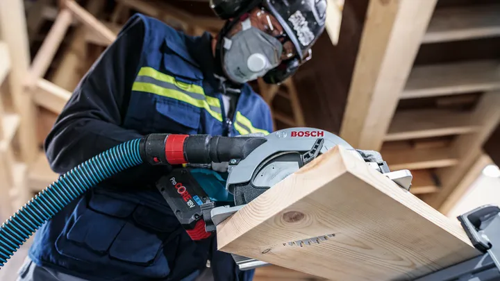 Una persona que usa equipo de seguridad corta una tabla de madera con una sierra circular.
