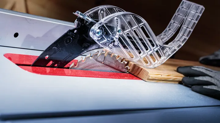 Sierra de mesa cortando madera, persona con equipo de seguridad guía el material.