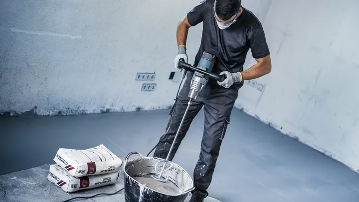 Una persona que usa equipo de seguridad mezcla cemento en polvo en un balde en un sitio de construcción.