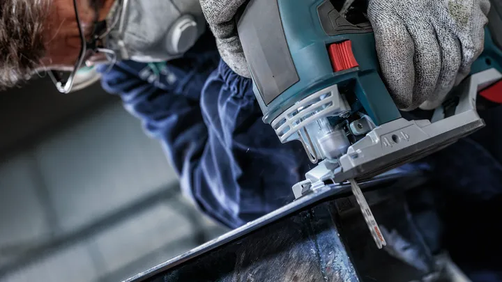 Una persona que usa equipo de seguridad utiliza una sierra caladora para cortar metal.