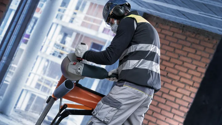 Una persona que usa equipo de seguridad corta un tubo de metal con una amoladora angular.