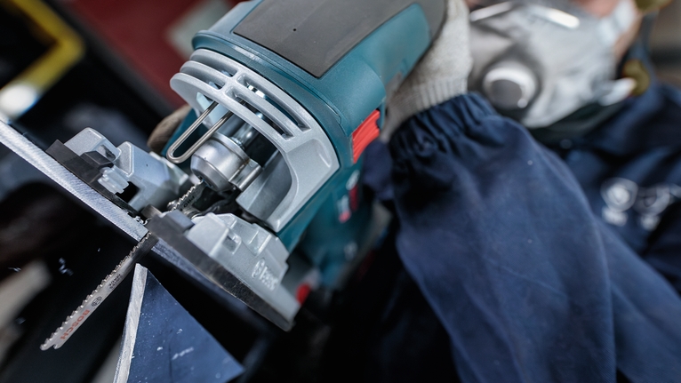 Persona que usa equipo de seguridad y utiliza una sierra caladora para cortar metal.