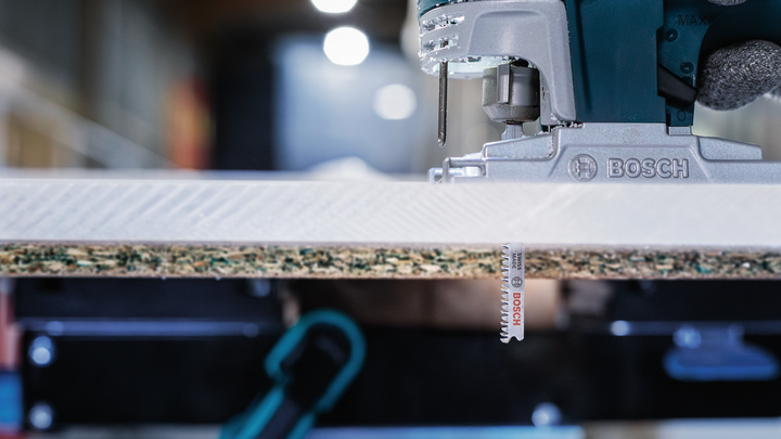 Una sierra caladora eléctrica cortando un trozo de madera laminada.