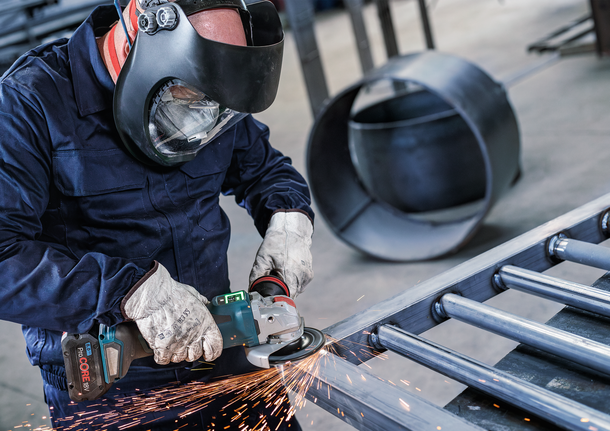 Una persona que usa equipo de seguridad muele metal, creando chispas.