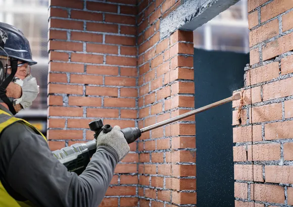 Una persona que usa equipo de seguridad cincela una pared de ladrillos con un martillo de demolición.