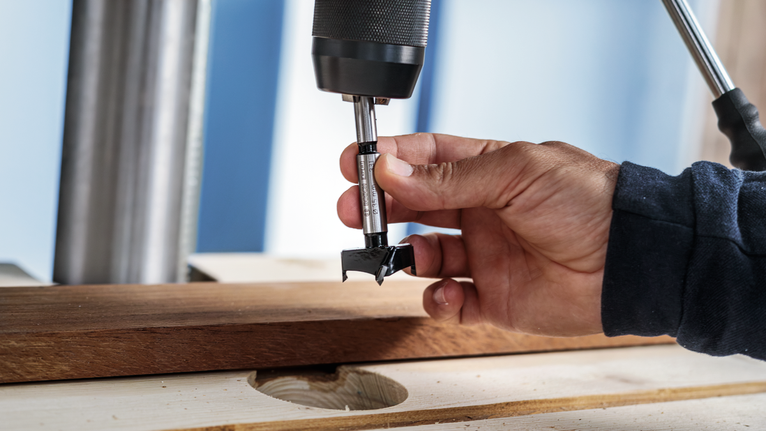 Persona que guía una broca para hacer un agujero en una tabla de madera.