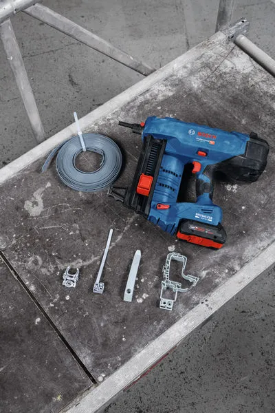 Clavadora de hormigón inalámbrica y accesorios de montaje colocados sobre un banco de trabajo.