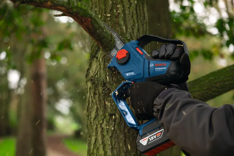 Una persona que usa equipo de seguridad poda la rama de un árbol usando una podadora inalámbrica.