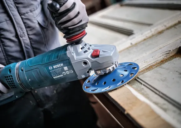 Una persona que usa equipo de seguridad utiliza una amoladora angular para lijar la superficie de una puerta de madera.