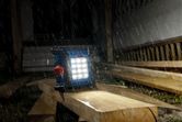 Luz de trabajo inalámbrica que ilumina tablones de madera bajo una intensa lluvia en un sitio de construcción.