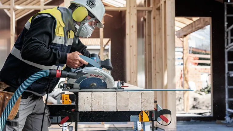 Una persona que lleva equipo de seguridad corta madera con una sierra circular en una obra en construcción.