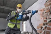 Una persona que usa equipo de seguridad utiliza un martillo demoledor con SDS max para romper una pared de ladrillos.