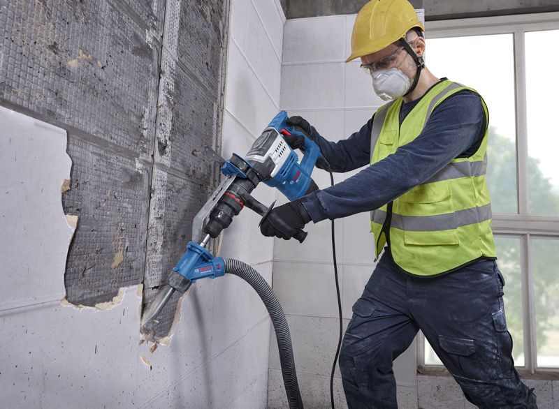 Un trabajador que usa equipo de seguridad utiliza un martillo demoledor con SDS max en una pared de azulejos.