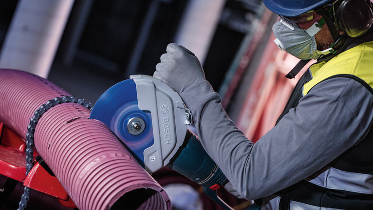 Una persona que usa equipo de seguridad corta un tubo grande de plástico con un cortador eléctrico.