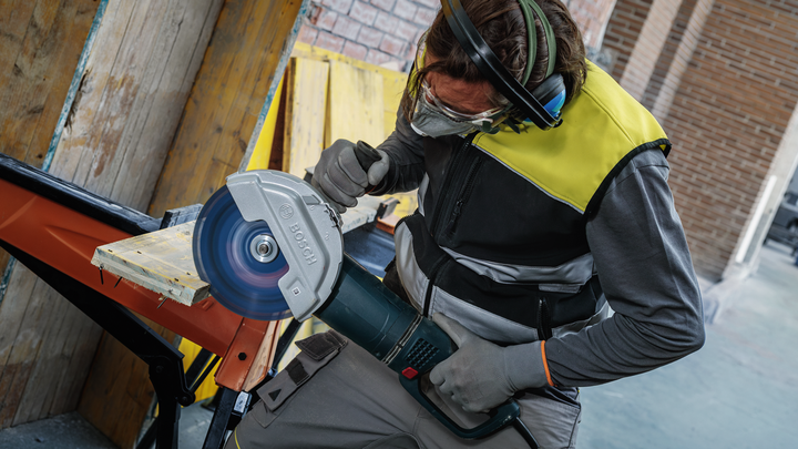 Una persona que usa equipo de seguridad corta una tabla de madera con una sierra circular grande.