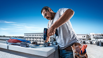 Un hombre trabaja en un techo con herramientas Bosch bajo un cielo azul claro.