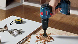 Un taladro Bosch Professional perfora una tabla con virutas de madera alrededor.